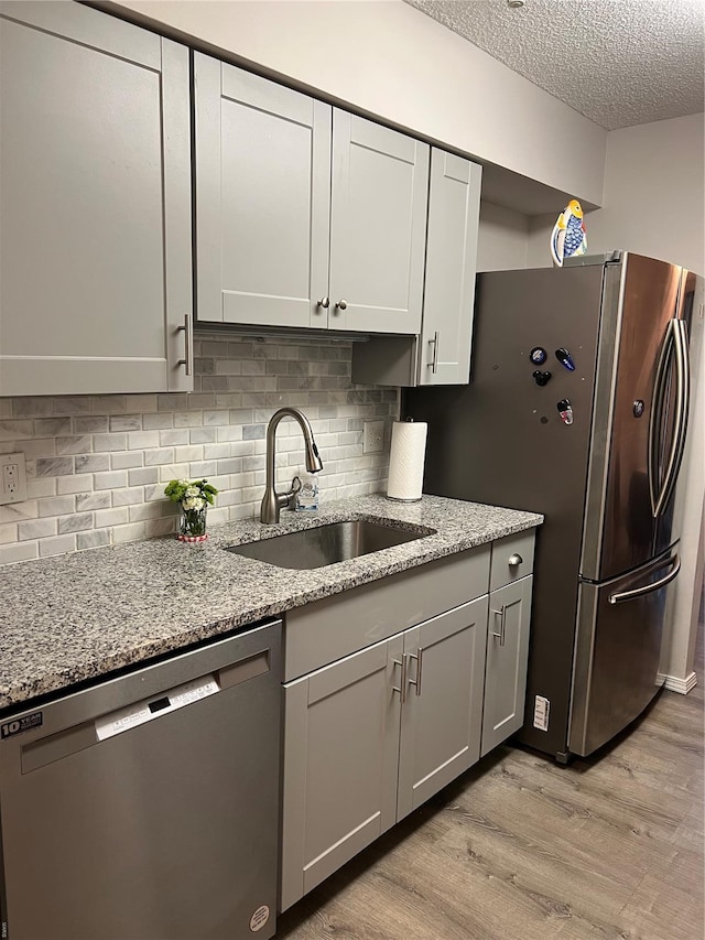 572 Coeur De Royale Unit 103, Creve Coeur, MO 63141 - kitchen featuring stainless steel dishwasher, a sink, a textured ceiling, light wood-type flooring, and light stone counters