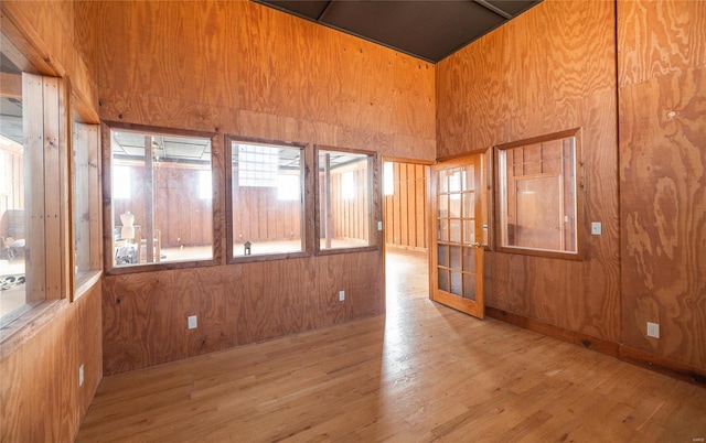 unfurnished room with wood finished floors, wood walls, plenty of natural light, and a high ceiling