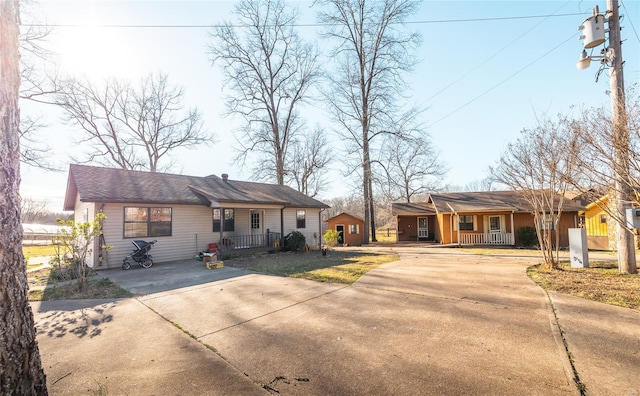 ranch-style home featuring a porch, concrete driveway, a storage unit, and an outbuilding