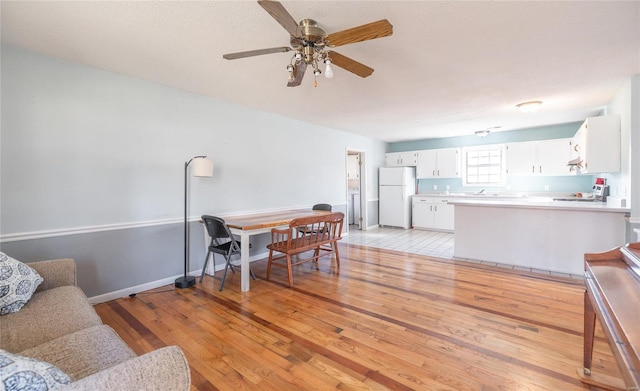 living room with light wood-type flooring, ceiling fan, and baseboards