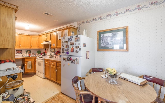 kitchen featuring white appliances, under cabinet range hood, a textured ceiling, wallpapered walls, and light countertops