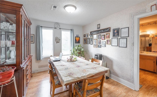 dining space featuring light wood-style flooring, a textured ceiling, and baseboards