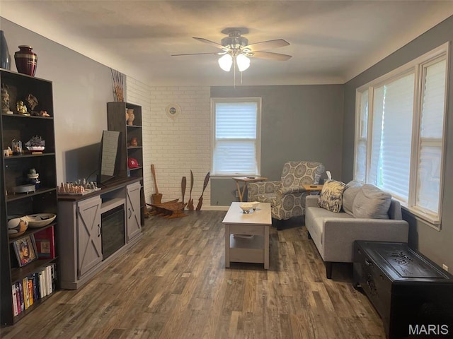living area with ceiling fan, dark wood-type flooring, and brick wall