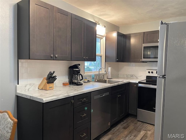 kitchen with stainless steel appliances, a sink, decorative backsplash, dark wood-style floors, and light countertops