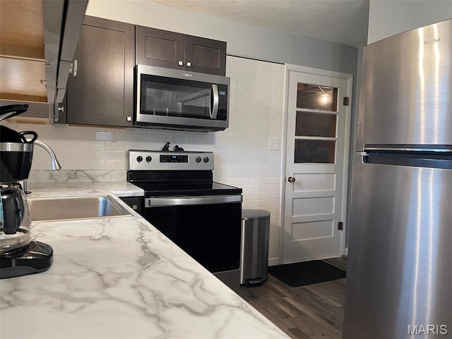 kitchen with stainless steel appliances, dark brown cabinets, a sink, dark wood-style flooring, and light stone counters