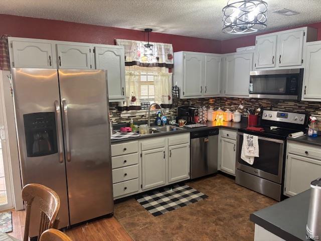 kitchen with stainless steel appliances, a sink, dark countertops, backsplash, and a textured ceiling