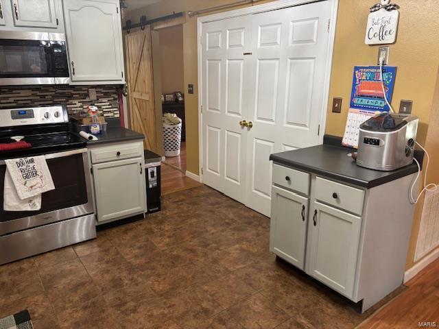 kitchen featuring stainless steel appliances, dark countertops, a barn door, backsplash, and white cabinets