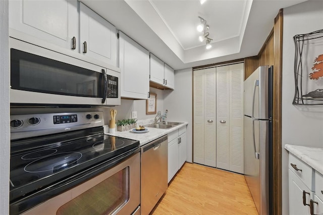 kitchen with stainless steel appliances, a sink, a tray ceiling, light wood-type flooring, and white cabinets