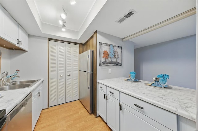 kitchen featuring stainless steel appliances, light wood-type flooring, a sink, a tray ceiling, and white cabinetry