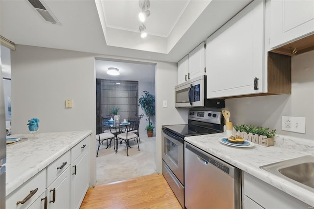 kitchen with appliances with stainless steel finishes, white cabinets, light wood-style floors, a sink, and ornamental molding