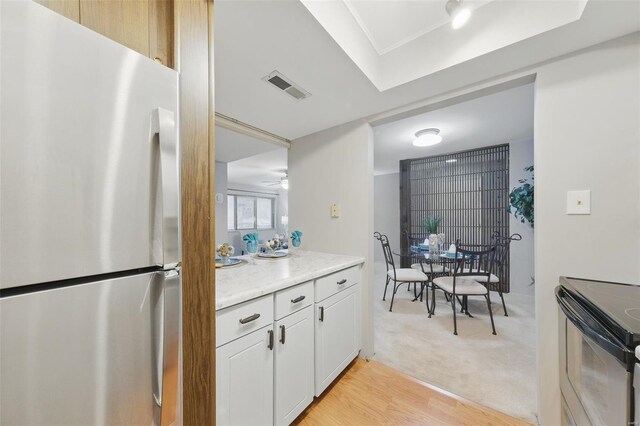 kitchen with freestanding refrigerator, black electric range, white cabinetry, light colored carpet, and ceiling fan
