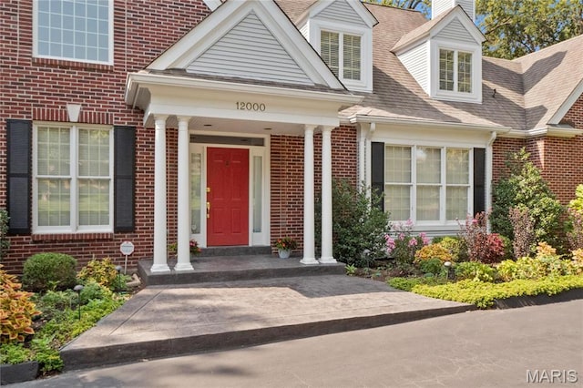 entrance to property featuring brick siding, roof with shingles, and a chimney