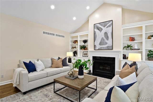 living room featuring wood finished floors, a fireplace with flush hearth, built in features, baseboards, and recessed lighting