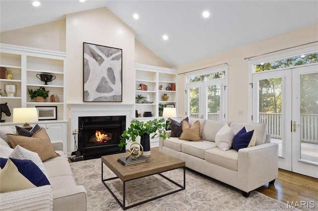 living area featuring vaulted ceiling, a fireplace with flush hearth, wood finished floors, recessed lighting, and built in shelves