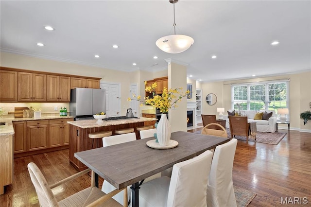 dining area featuring a fireplace with flush hearth, recessed lighting, ornamental molding, and wood finished floors