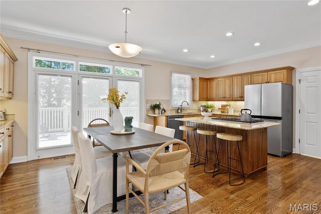 kitchen with appliances with stainless steel finishes, a kitchen island, crown molding, tasteful backsplash, and wood finished floors