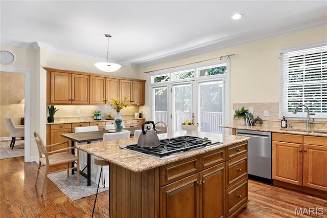 kitchen featuring a sink, stainless steel appliances, light wood finished floors, tasteful backsplash, and ornamental molding