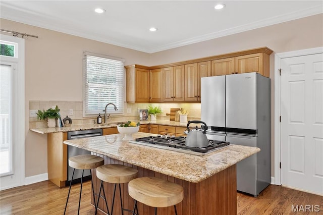 kitchen featuring stainless steel appliances, a center island, light wood-type flooring, a sink, and a kitchen breakfast bar