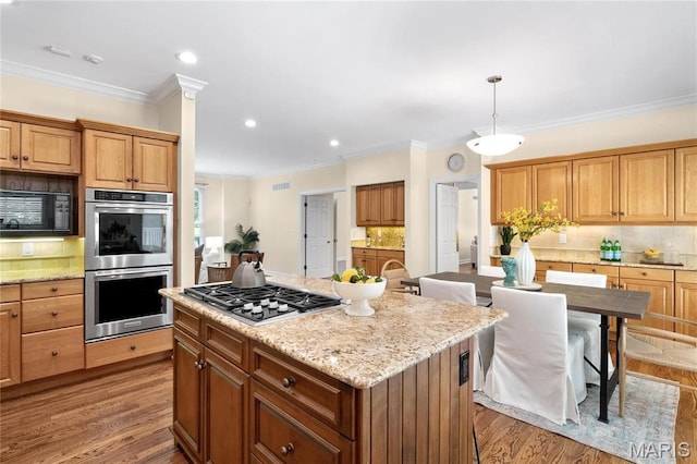 kitchen with appliances with stainless steel finishes, backsplash, a kitchen island, light wood finished floors, and crown molding