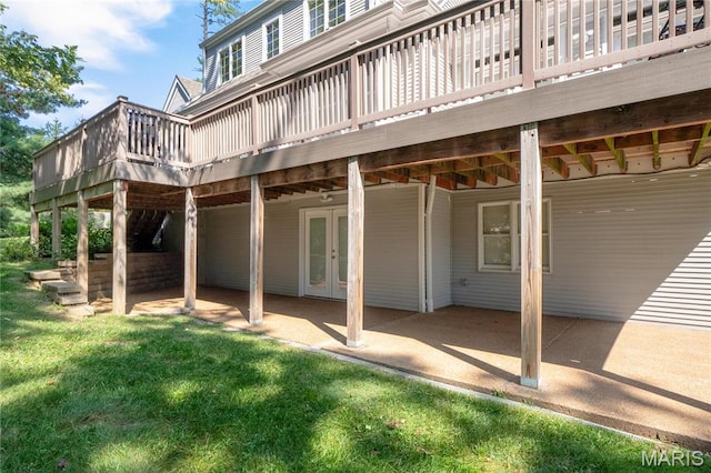 rear view of house featuring french doors, a wooden deck, a patio, and a lawn