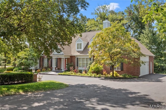 view of front of house with brick siding, driveway, a garage, and a chimney