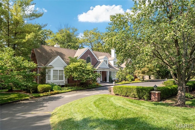 view of front of house featuring asphalt driveway, a front yard, and a chimney