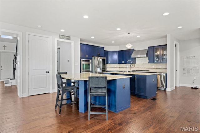 351 Oak Stand Ct, Chesterfield, MO 63005 - kitchen featuring appliances with stainless steel finishes, an island with sink, blue cabinets, wall chimney range hood, and recessed lighting