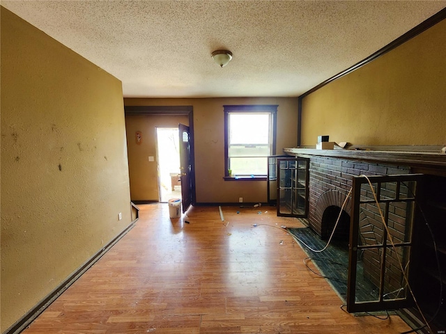 4052 Detonty St, Saint Louis, MO 63110 - unfurnished living room with a textured wall, light wood finished floors, a textured ceiling, a brick fireplace, and baseboards