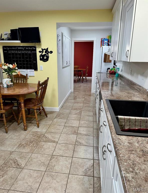 kitchen with a sink, white cabinets, baseboards, and light tile patterned floors