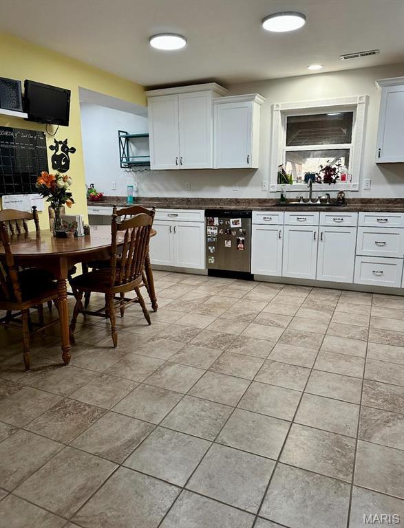 kitchen with stainless steel dishwasher, dark countertops, a sink, white cabinets, and light tile patterned floors