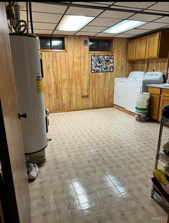 finished below grade area featuring electric water heater, independent washer and dryer, wooden walls, and a paneled ceiling