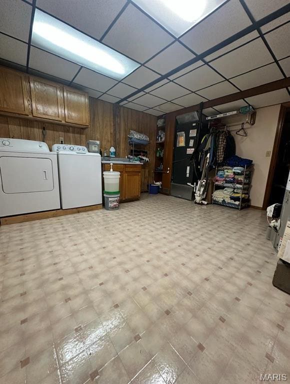finished below grade area featuring washing machine and clothes dryer, a drop ceiling, light flooring, and wooden walls
