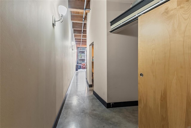 hall featuring baseboards and finished concrete flooring