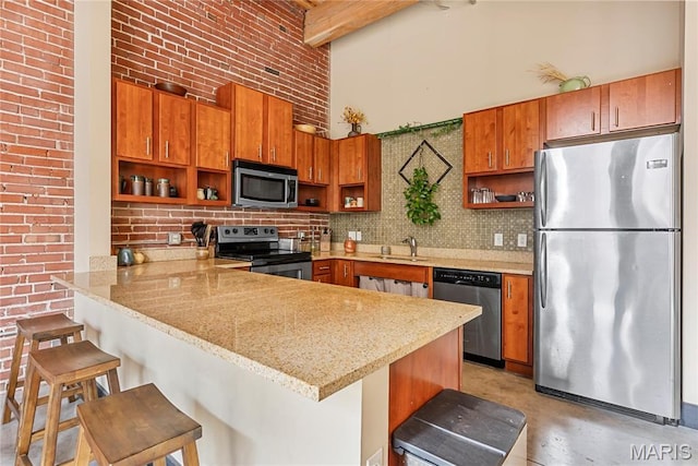 1123 Washington Ave Unit 305, Saint Louis, MO 63101 - kitchen featuring appliances with stainless steel finishes, open shelves, a peninsula, brown cabinets, and a towering ceiling