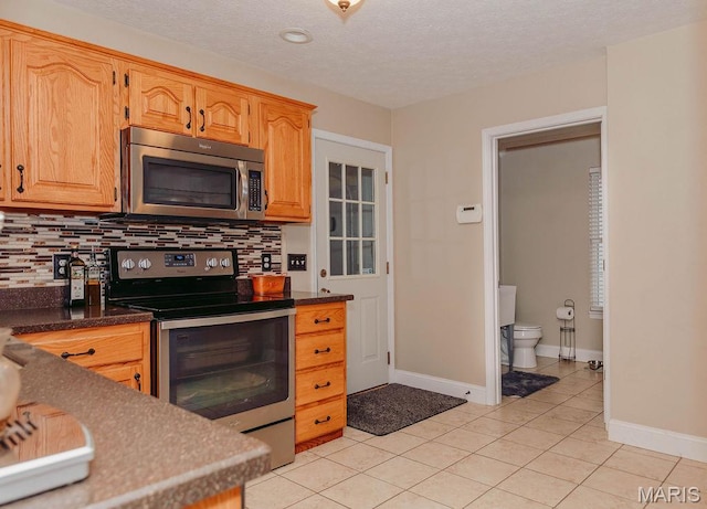 17145 Lensman Rd, Saint Robert, MO 65584 - kitchen featuring appliances with stainless steel finishes, light tile patterned flooring, backsplash, baseboards, and a textured ceiling