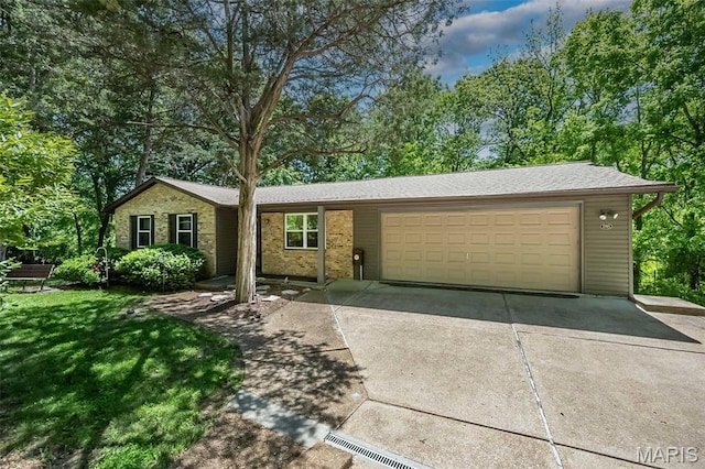 ranch-style house featuring an attached garage, concrete driveway, a front yard, and view of wooded area