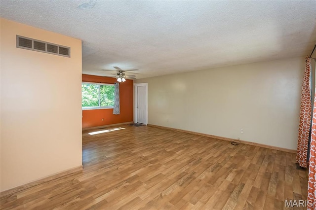 spare room featuring light wood-type flooring, a ceiling fan, a textured ceiling, and baseboards