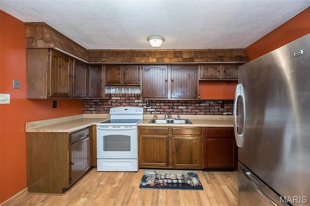 kitchen with freestanding refrigerator, electric stove, a sink, light countertops, and light wood-style flooring