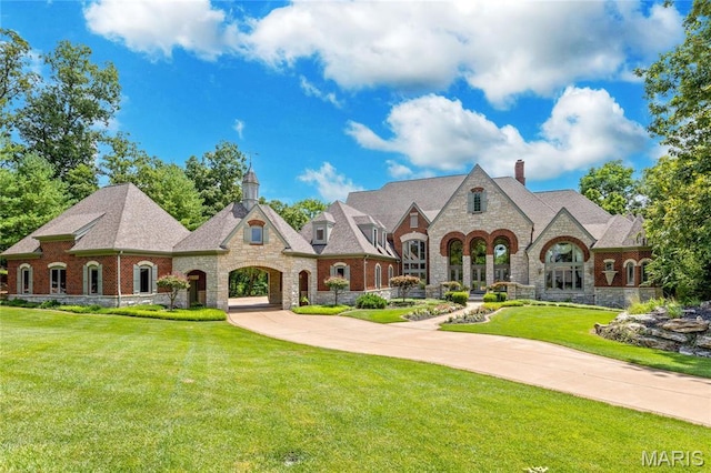 french provincial home featuring stone siding, a chimney, a front lawn, and driveway
