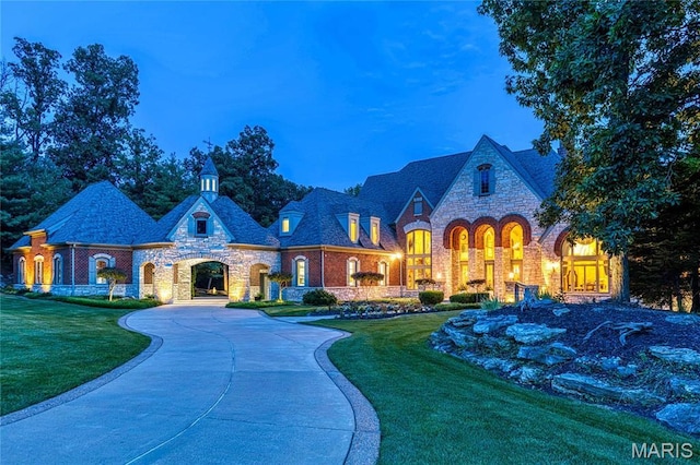 view of front of house with stone siding, a front yard, curved driveway, and brick siding