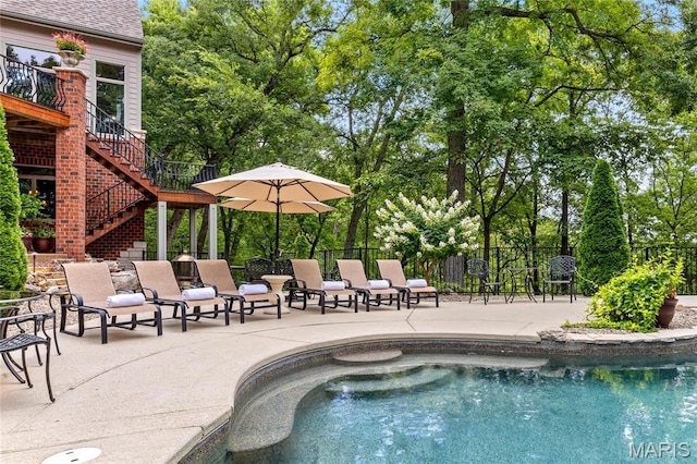 view of swimming pool with stairs, fence, a patio, and view of scattered trees