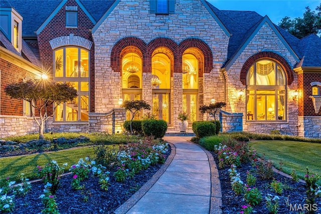 view of front of house featuring stone siding, brick siding, a high end roof, and a front lawn