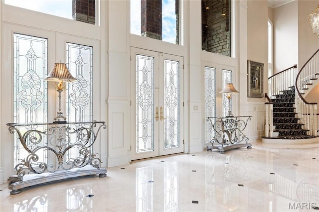 entrance foyer featuring a high ceiling, a decorative wall, stairway, french doors, and a chandelier