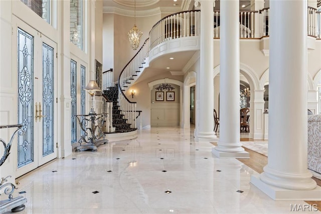 entrance foyer featuring a high ceiling, ornate columns, stairway, ornamental molding, and arched walkways