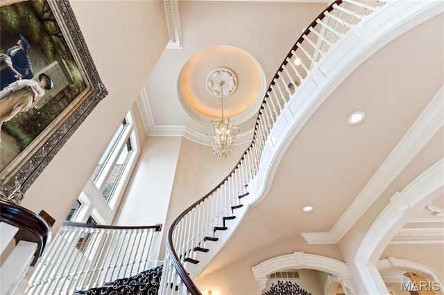 stairs featuring a towering ceiling, a chandelier, crown molding, arched walkways, and recessed lighting