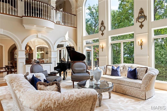 living room with a towering ceiling, plenty of natural light, decorative columns, a decorative wall, and arched walkways
