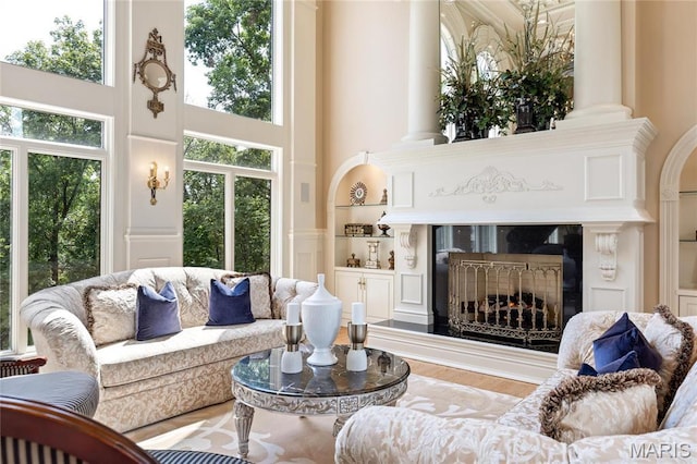 living area with a high ceiling, a fireplace, built in shelves, and wood finished floors