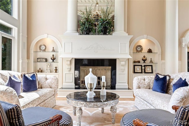 living room featuring decorative columns, built in shelves, a fireplace with raised hearth, and a towering ceiling