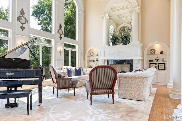 sitting room featuring a high ceiling, ornate columns, built in shelves, a fireplace, and light wood finished floors