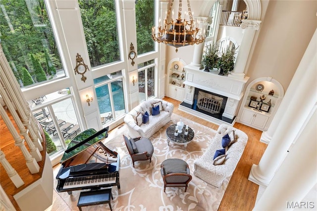 living room with a towering ceiling, ornate columns, healthy amount of natural light, a chandelier, and wood finished floors